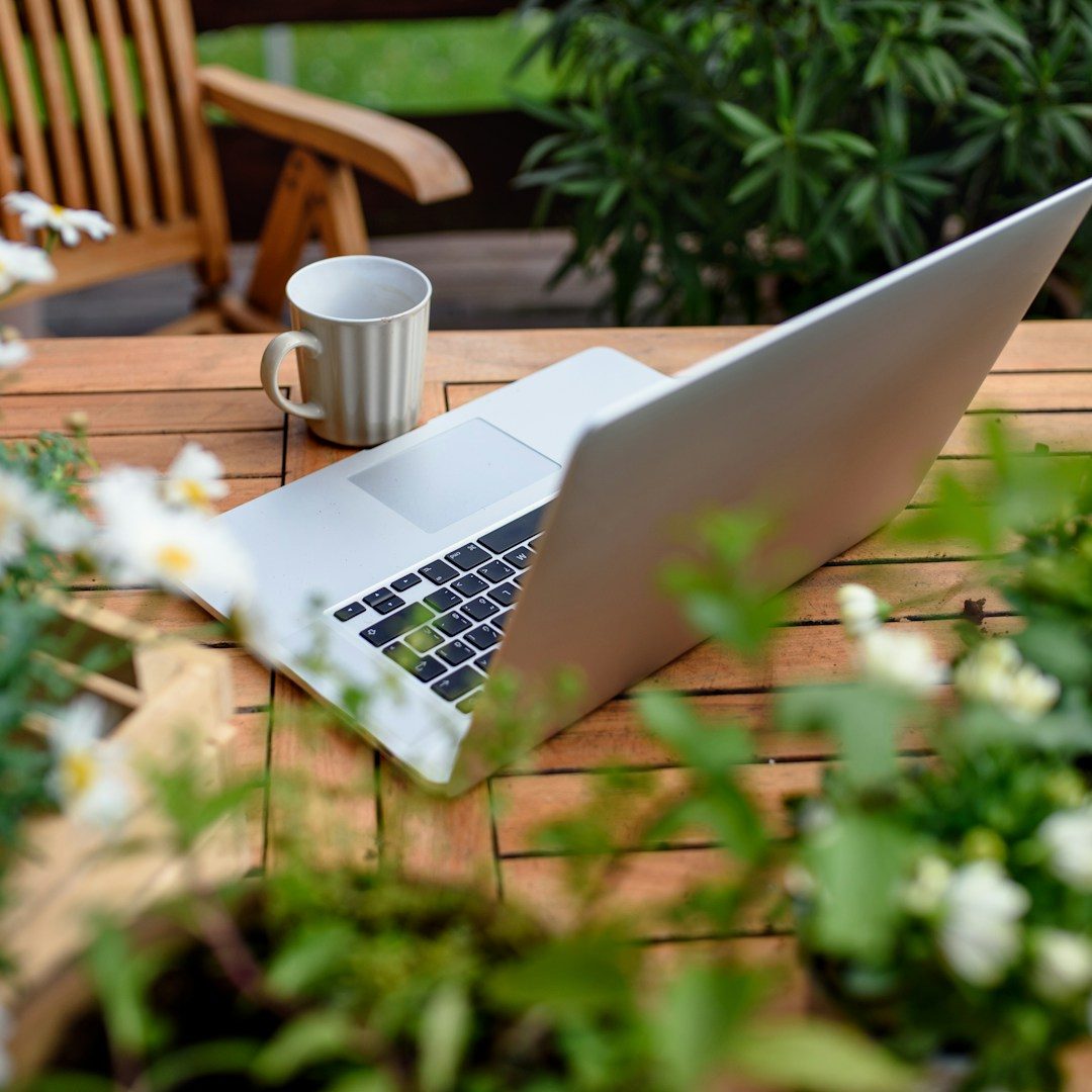 Laptop and notebook on wooden table surrounded by greenery — symbolizing reflection, focus, and intentional growth.
